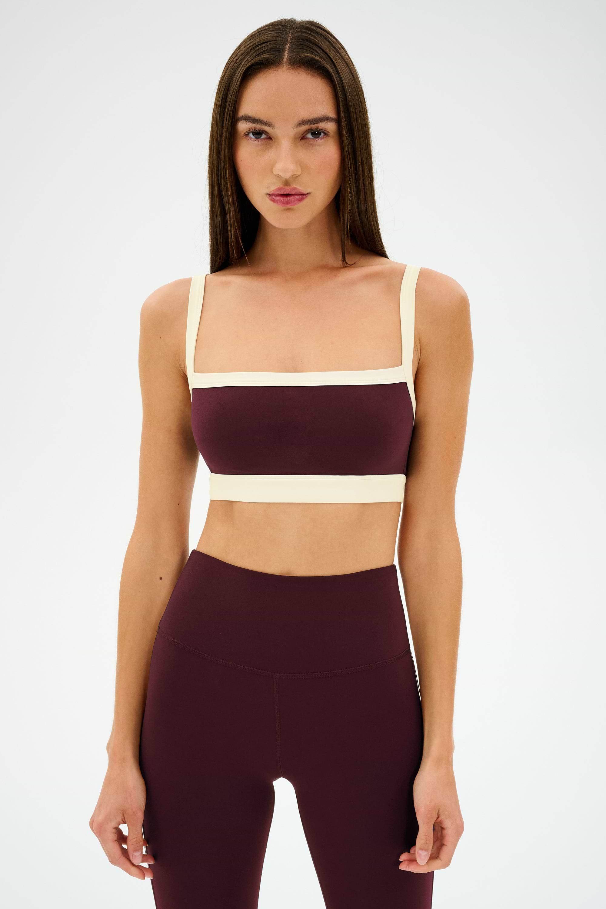 A woman faces forward against a white background, wearing the SPLITS59 Monah Rigor Bra in Dark Cherry/Creme with matching high-waisted leggings.