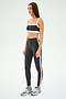 A woman confidently poses in a SPLITS59 Monah Rigor Bra in graphite/white and silver sneakers against a plain background, capturing the essence of gym workouts.