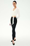 A person stands slightly angled, wearing the SPLITS59 Bella Airweight Lite Wrap in white with black leggings and ballet flats, set against a plain white background.