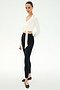 A person stands slightly angled, wearing the SPLITS59 Bella Airweight Lite Wrap in white with black leggings and ballet flats, set against a plain white background.