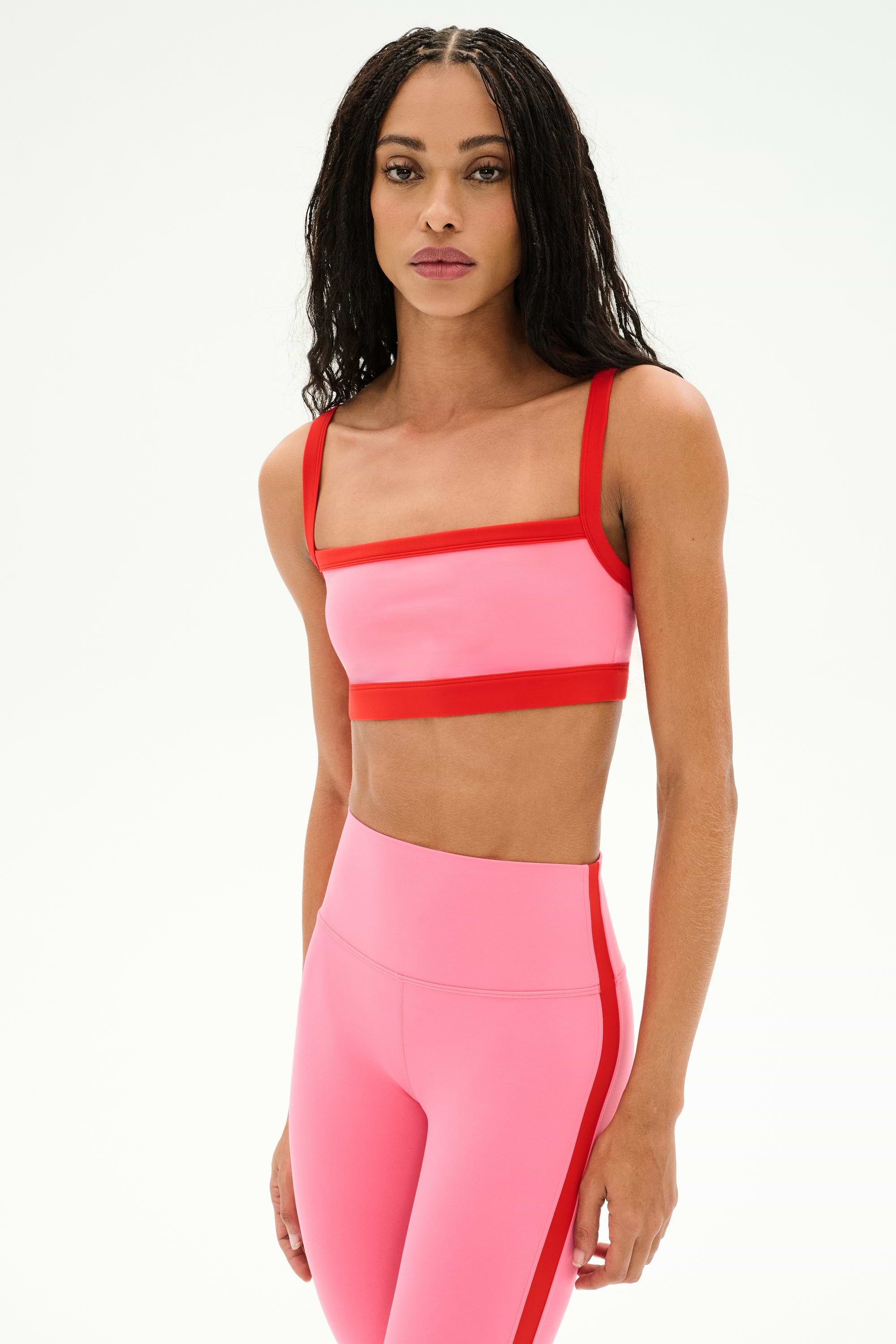 A person stands against a plain white background wearing the SPLITS59 Monah Rigor Bra in Strawberry/Lotus Red with matching high-waisted leggings.