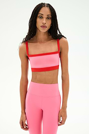 A woman wearing a SPLITS59 Monah Rigor Bra in Strawberry/Lotus Red and matching high-waisted leggings stands against a plain white background.