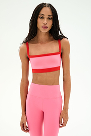 A woman wearing a SPLITS59 Monah Rigor Bra in Strawberry/Lotus Red and matching high-waisted leggings stands against a plain white background.