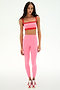 A woman poses against a plain background in SPLITS59's Clare High Waist Rigor 7/8 leggings in Strawberry/Lotus Red paired with a matching sports bra and red-and-white sneakers—an ideal outfit for gym workouts.