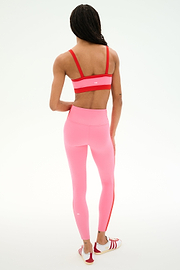 A person stands facing away, wearing a SPLITS59 Monah Rigor Bra in Strawberry/Lotus Red, high-waisted pink leggings, and red-and-white athletic shoes against a plain white background.