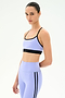 A woman wears the SPLITS59 Emerson Airweight Bra in Purple Haze/Black, made from stretch fabric, paired with high-waisted leggings, standing against a plain white background.