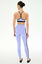 A woman stands with her back to the camera, wearing SPLITS59’s Ella High Waist Airweight 7/8 leggings in Purple Haze/Black, featuring black side stripes, set against a plain light background.