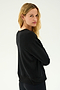 A woman with long blonde hair is wearing the SPLITS59 Sonja Fleece Sweatshirt in black paired with matching pants, standing against a light background and looking over her shoulder.