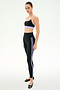 A woman stands on a white background wearing the SPLITS59 Emerson Airweight Bra in Black/Purple Haze, paired with high-waisted black leggings with light blue stripes and black ballet flats.