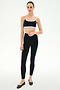 A woman stands against a white background wearing the SPLITS59 Emerson Airweight Bra in Black/Purple Haze, paired with high-waisted black nylon leggings featuring side stripes and black ballet flats.