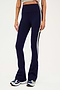 Front view of woman wearing dark blue high waist below ankle length legging with wide flared bottoms and white and black side stripes on both legs. Paired with gray,black and bright blue shoes.