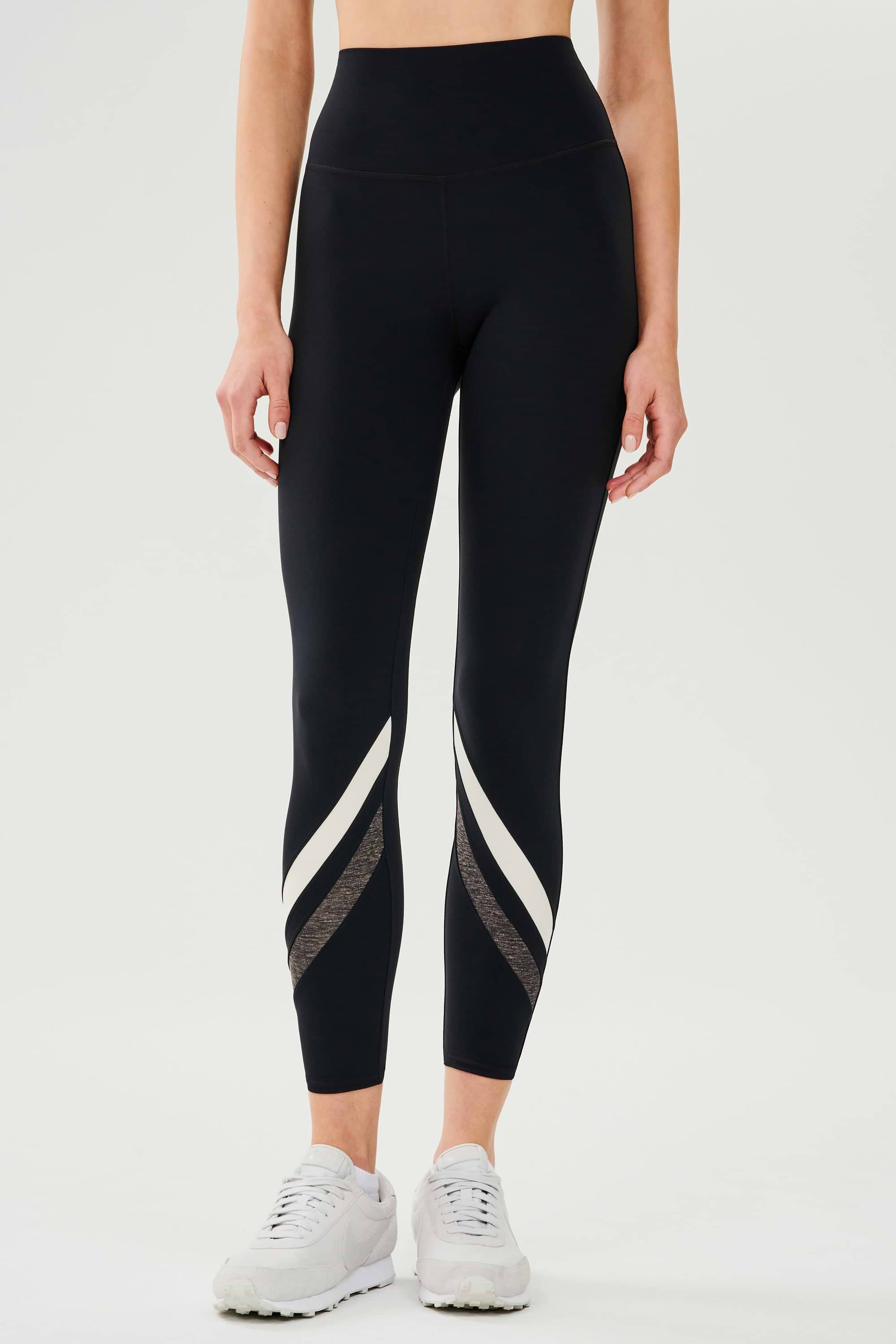 Front view of girl wearing black leggings with two white and grey stripes across the shin with white shoes