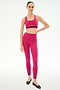 A person stands against a plain background wearing the SPLITS59 Miles High Waist Rigor 7/8 leggings in Sangria/Black, paired with a matching bright pink sports bra and black flats.