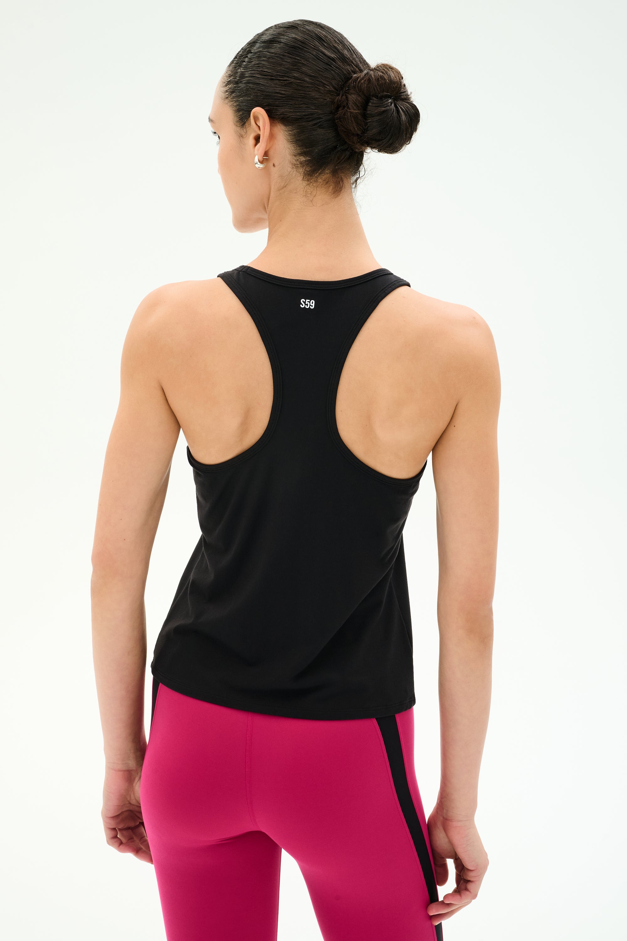A woman faces away wearing the SPLITS59 Mel Airweight Lite Tank in black, ideal for Pilates, paired with bright pink leggings featuring a black stripe, set against a plain light background.