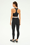 Dressed in SPLITS59's Bailey Active Rib Bralette in Heather Graphite, a woman stands with her back to the camera. She pairs the bralette with leggings and sneakers, perfectly poised for her Pilates session.