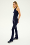 A woman stands against a plain background, wearing a black sleeveless top, the SPLITS59 Raquel High Waist Flared Legging in Indigo made from 4-way stretch supplex fabric, and black and white athletic shoes. She has long blonde hair and is looking towards the camera, embodying the Raquel yoga style.