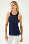 A woman with long blonde hair wearing the SPLITS59 Kiki Rib Tank Full Length in Indigo and white pants stands against a plain background, embodying the elegance of yoga.
