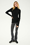 A person with long hair stands wearing a black turtleneck top, Raquel High Waist Flared Legging in Heather Grey/White/Black from SPLITS59, and black shoes, with one hand on their hip.