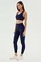 A woman stands wearing a navy blue sports bra, SPLITS59 Airweight High Waist Legging in Indigo, and white athletic shoes, posing against a plain light background.