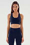 A person with long hair, dressed in an indigo Sara Airweight Bra by SPLITS59 and black leggings, stands poised against a plain light background, ready for a session of hot yoga or Pilates.