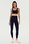 A person standing and wearing the SPLITS59 Ella Airweight Bra in Black/White paired with matching leggings featuring white side stripes and white sneakers, set against a plain background.