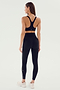 A person stands facing away, wearing the SPLITS59 Ella Airweight Bra in Black/White, high-waisted black leggings with white stripes, and white athletic shoes, ready for a hot yoga session.
