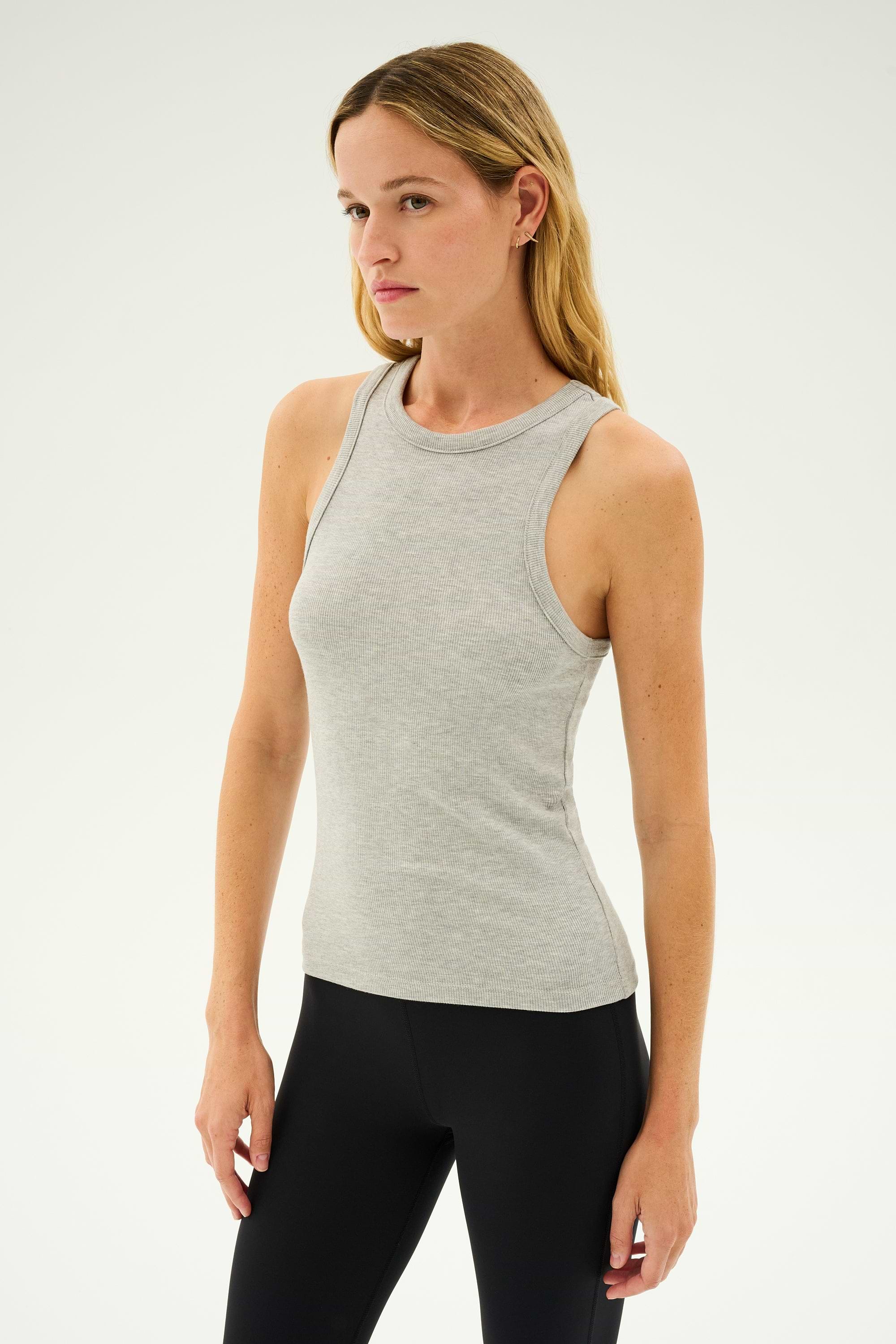 A person with long hair wearing the SPLITS59 Kiki Rib Tank Full Length in Heather Grey and black pants, standing against a plain background, ready for yoga.