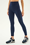 An individual wearing SPLITS59's Airweight Super High Waist 7/8 leggings in Indigo paired with black New Balance sneakers stands against a plain background. The person's head is not visible in the image, hinting that they might be preparing for a hot yoga session.