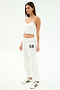 A woman poses in a white studio wearing the SPLITS59 Airweight Crop - White, matching drawstring pants with "59" on the left leg, and white sneakers with navy stripes—ideal for hot yoga or a casual outing.