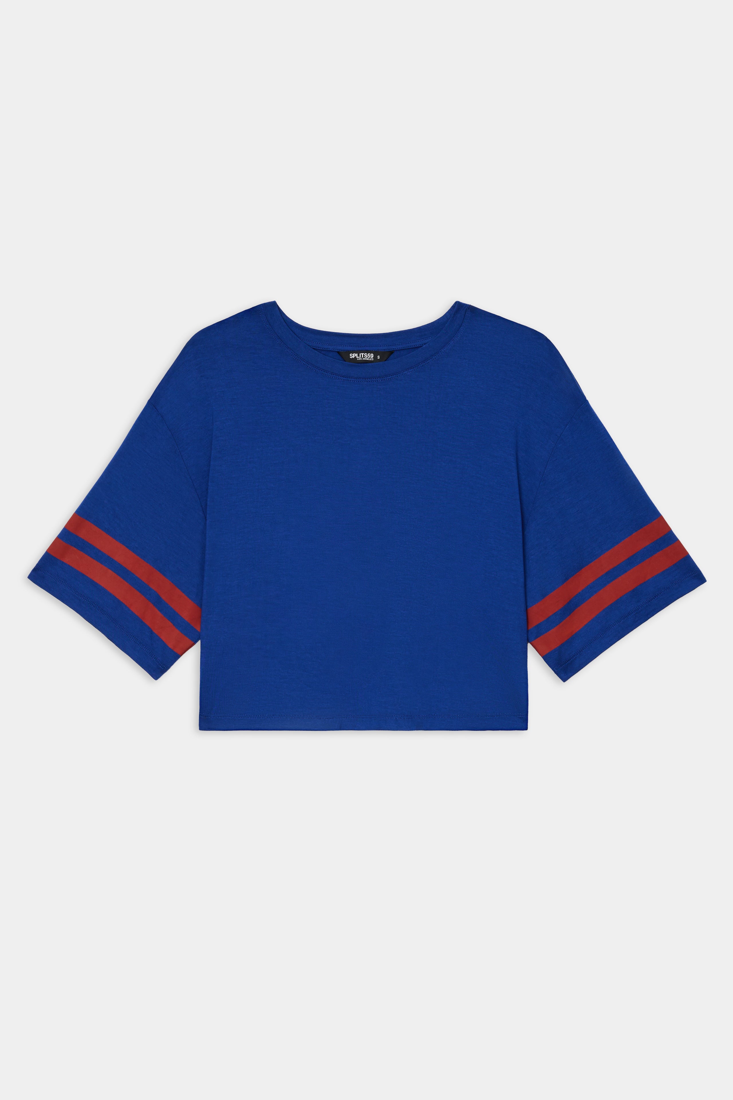 The SPLITS59 Djuna Oversized Crop Jersey Tee - Cobalt/Terracotta is a blue, stretchy, short-sleeve crop top with red stripes on the sleeves, shown on a white background.