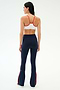 A woman faces away wearing the SPLITS59 Loren Seamless Bra in White/Lotus Red, paired with high-waisted navy flared leggings featuring red side stripes—an ideal yoga or gym outfit on a plain light background.