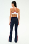 A woman faces away wearing the SPLITS59 Loren Seamless Bra in White/Lotus Red, paired with high-waisted navy flared leggings featuring red side stripes—an ideal yoga or gym outfit on a plain light background.