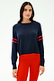 A woman stands against a plain light background wearing the SPLITS59 Brooks Stripe Fleece Sweatshirt, a navy long-sleeve top with red striped sleeves, paired with bright red leggings.