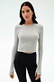 A woman faces forward in the SPLITS59 Louise Rib Long Sleeve Crop in Heather Grey, styled with black high-waisted leggings—an ideal workout top—against a plain white background.