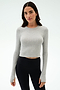 A woman faces forward in the SPLITS59 Louise Rib Long Sleeve Crop in Heather Grey, styled with black high-waisted leggings—an ideal workout top—against a plain white background.