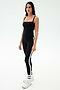 A woman stands against a plain background wearing the SPLITS59 Monah Rigor Tank in black, paired with black leggings featuring white side stripes, along with white socks and sneakers—ideal for gym workouts.