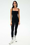 A woman stands against a plain background wearing the SPLITS59 Monah Rigor Tank in black, paired with black leggings, white athletic shoes, and white socks with black stripes—ideal for gym workouts.