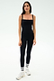 A woman stands against a plain background wearing the SPLITS59 Monah Rigor Tank in black, paired with black leggings, white athletic shoes, and white socks with black stripes—ideal for gym workouts.