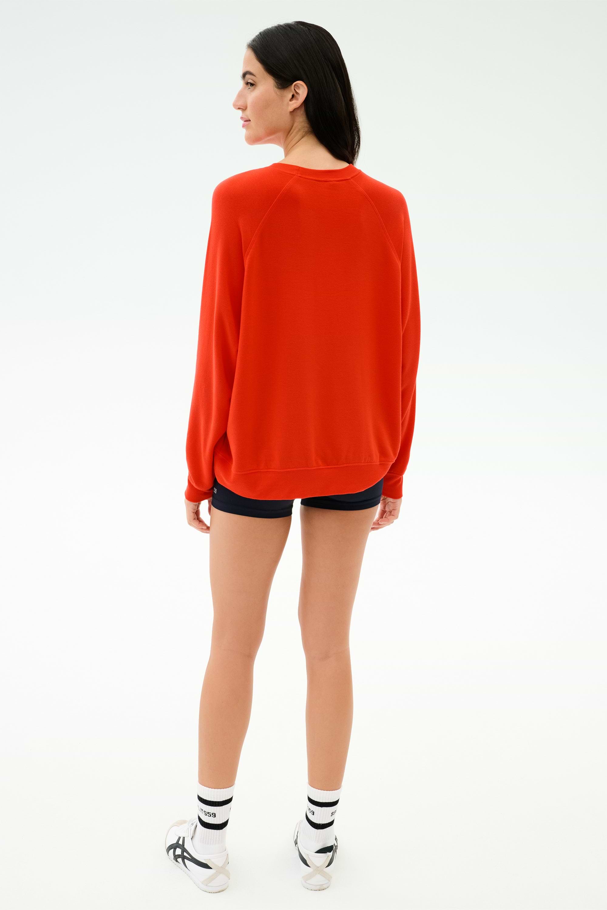 Person stands with their back to the camera in the SPLITS59 Andie Oversized Fleece Sweatshirt in Lotus Red, paired with black shorts and white sneakers. Made in Los Angeles for comfort and style against a plain white background.