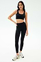 A woman stands on a white background wearing the black SPLITS59 Sprint Rigor Bra, paired with black high-waisted leggings and white sneakers.