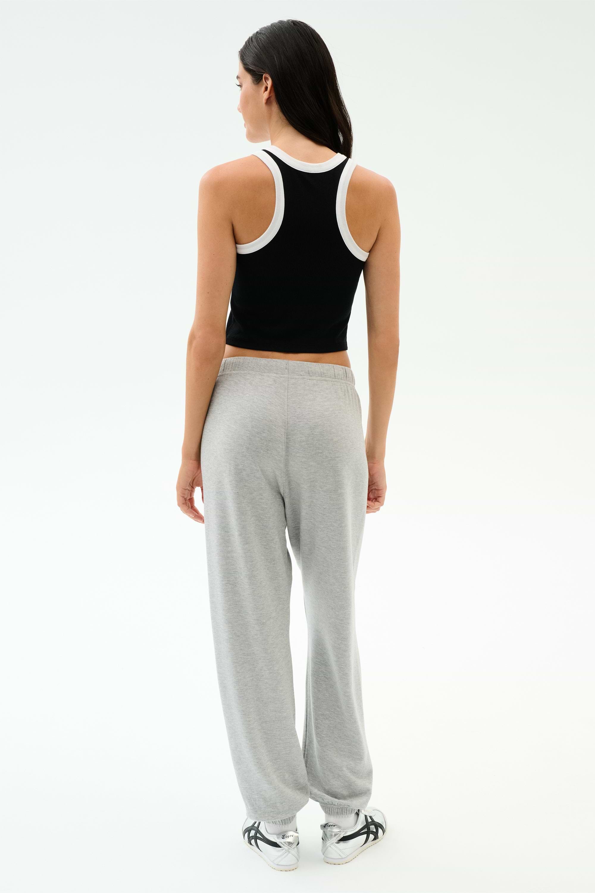A woman faces away, wearing the SPLITS59 Kiki Rib Crop Tank in Black/White with light gray sweatpants and white sneakers, set against a plain white background.