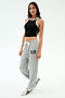 A woman wears the SPLITS59 Kiki Rib Crop Tank in Black/White with light gray sweatpants featuring "59" on the leg and white athletic shoes, set against a plain white background—ideal for gym or casual wear.