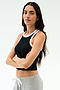 A woman with long brown hair stands with arms crossed, wearing the SPLITS59 Kiki Rib Crop Tank in Black/White and light gray sweatpants, perfect for gym workouts, against a plain white background.