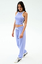 A woman stands against a white background wearing SPLITS59’s Andie Oversized Fleece Sweatpant in Purple Haze, paired with a light purple crop top and white sneakers—ideal for warm weather workouts.