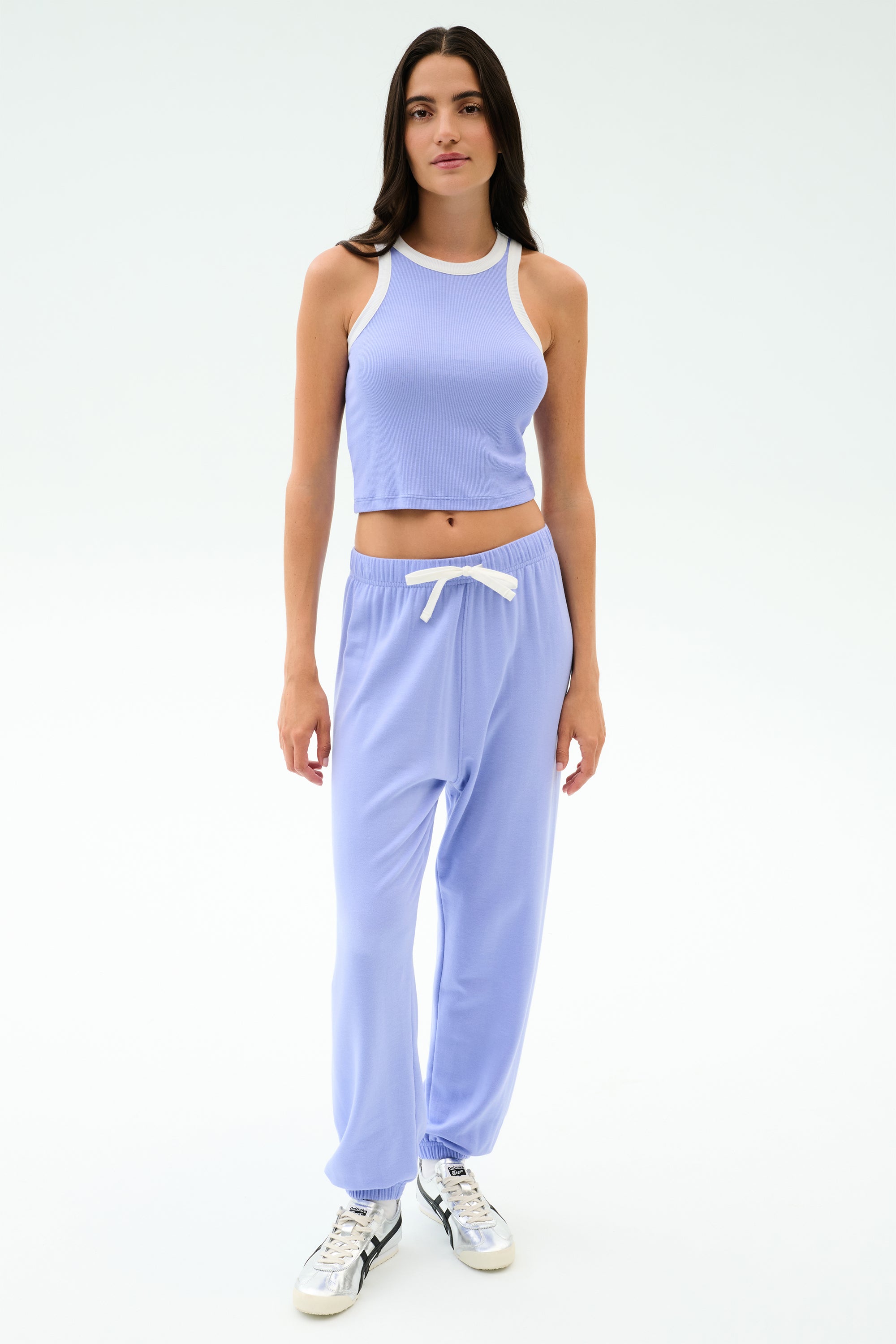 A person stands facing forward in the SPLITS59 Andie Oversized Fleece Sweatpant in Purple Haze, styled with a lavender crop top and white sneakers—an ideal outfit for warm weather workouts.