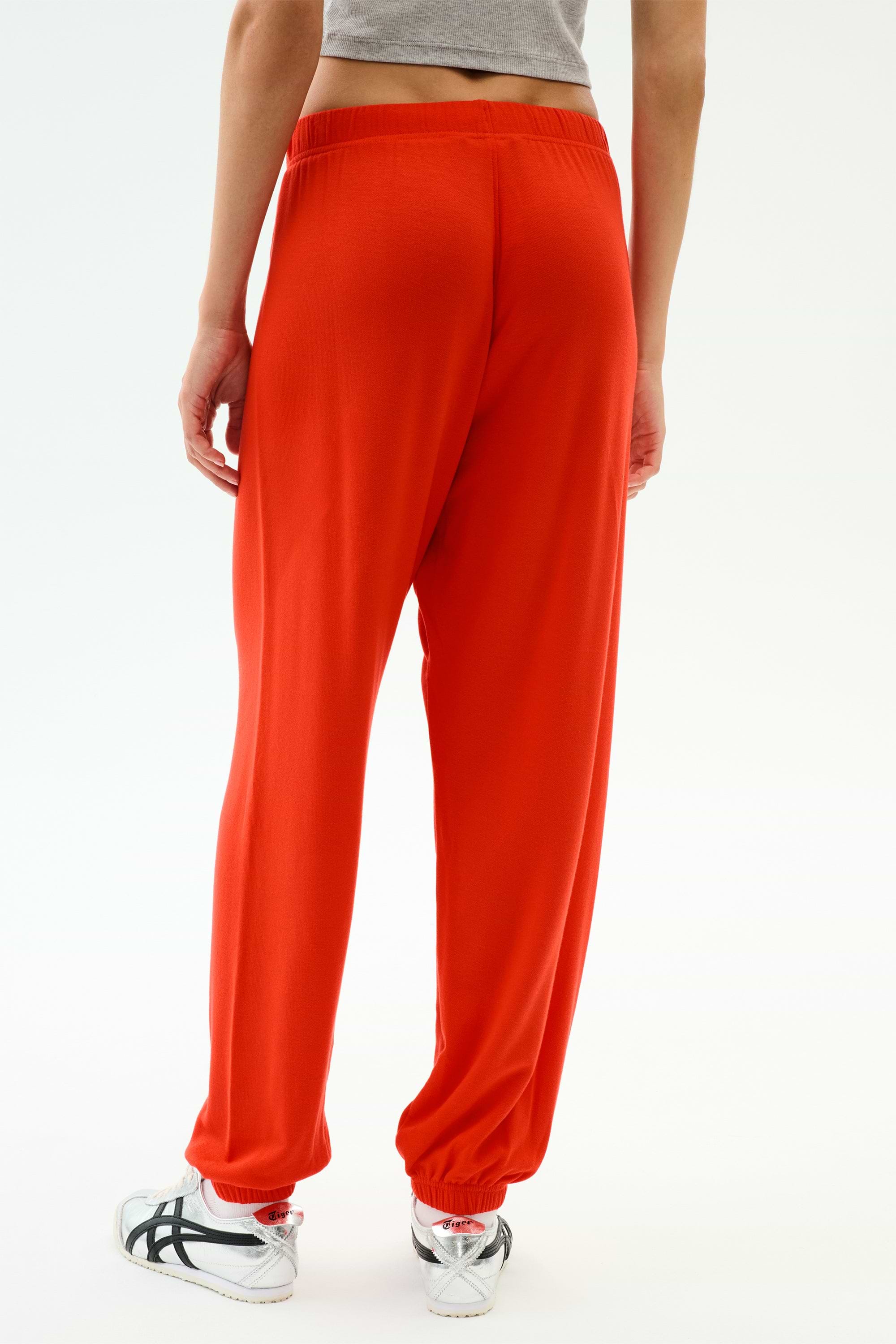 A person wears the SPLITS59 Andie Oversized Fleece Sweatpant in Lotus Red with a gray crop top and white athletic shoes, standing against a plain light background—a vibrant, comfortable choice for warm weather workouts.