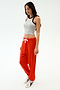 Woman standing against a white background wearing a grey sleeveless crop top, SPLITS59 Andie Oversized Fleece Sweatpant in Lotus Red, and white sneakers—ideal for warm weather workouts.