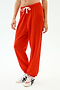 A person wears SPLITS59's Andie Oversized Fleece Sweatpant in Lotus Red with a white drawstring and white sneakers with black stripes, ideal for warm weather workouts, standing against a plain white background.