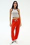 A woman stands against a white background wearing the SPLITS59 Kiki Rib Crop Tank in Heather Grey/Black, red sweatpants with a white drawstring, and white athletic shoes.