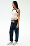 A woman wears the SPLITS59 Kiki Rib Crop Tank in White/Indigo with navy drawstring pants and silver athletic shoes—an easy, gym-ready look against a simple light background.
